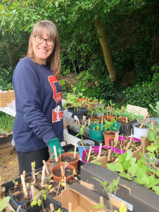 Woman in gardening gloves standing with trays of seedlings.